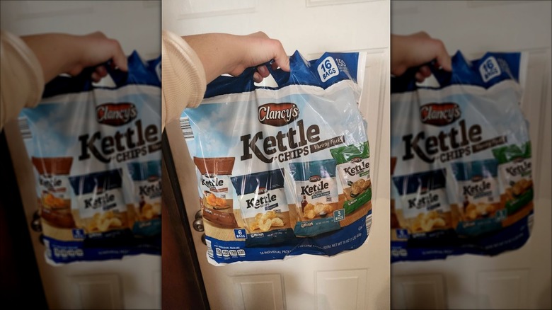 A hand holds a multi-pack of Aldi kettle chips by the bag handle