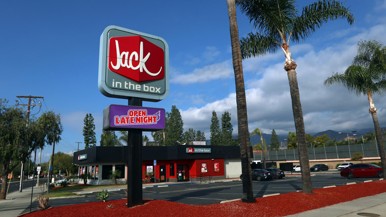 The exterior and sign of a Jack in the Box restaurant surrounded by palm trees