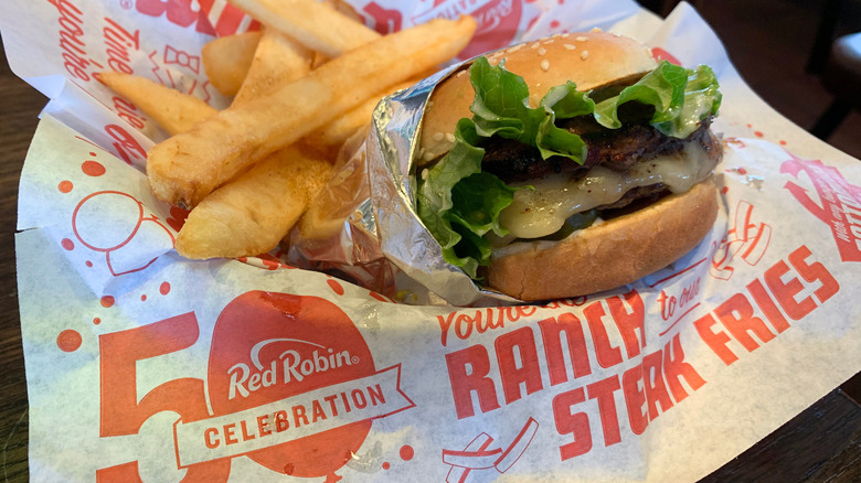A cheeseburger and steak fries sit on food-safe paper branded with the Red Robin restaurant's 50th anniversary celebration logo