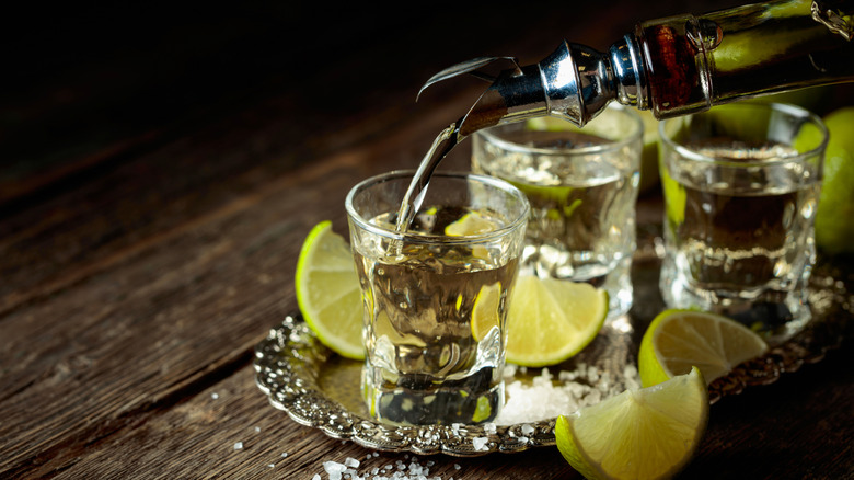 Pouring tequila into shot glasses with lime wedges and salt