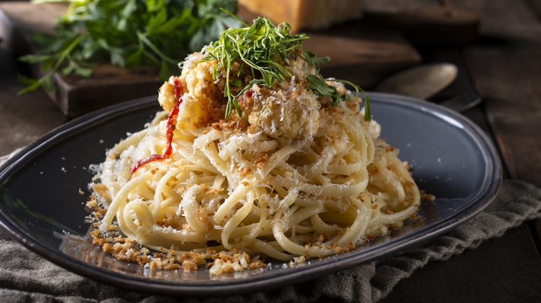 A black plate of fettuccine topped with breadcrumbs