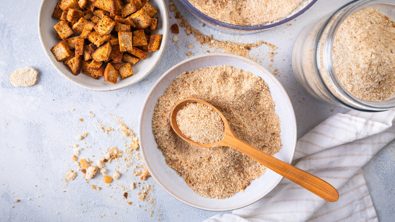 Bowl of breadcrumbs with spoon beside a bowl of croutons