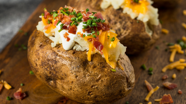 Closeup of a loaded baked potato on a wooden cutting board