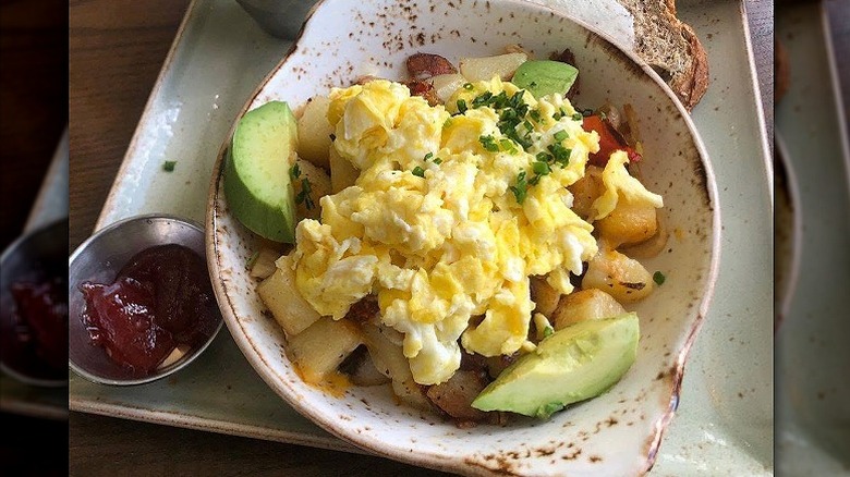 Scrambled eggs sit on top of an avocado and potato hash at First Watch