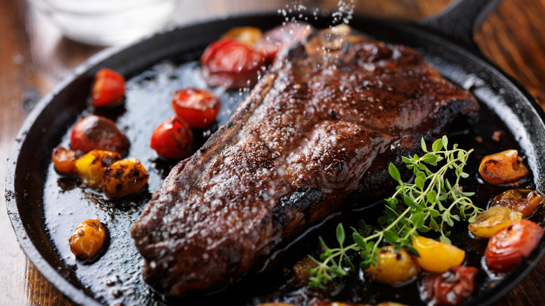 Closeup of a New York strip steak on a cast iron platter with herbs and tomatoes