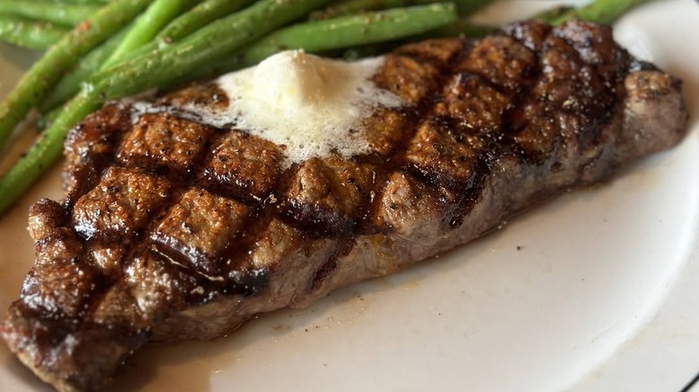 Closeup of a New York strip steak with butter and green beans at Saltgrass Steak House