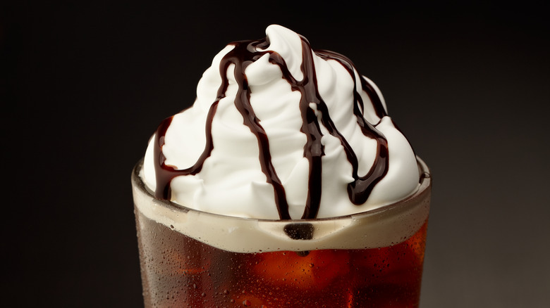 Brown beverage in a glass topped with whipped cream and chocolate syrup