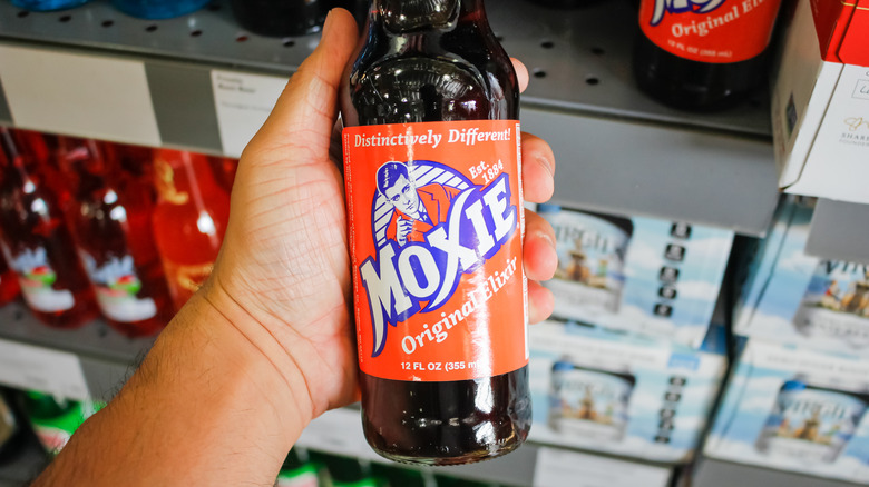 Hand holding a bottle of Moxie soda in a store