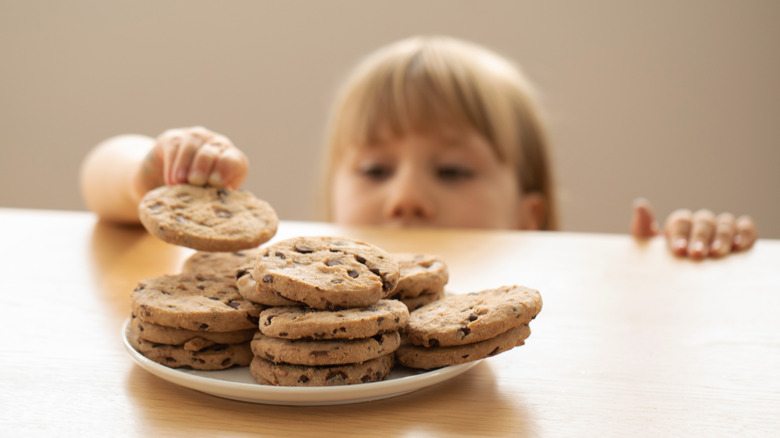 Child taking cookie from a plate of cookies.