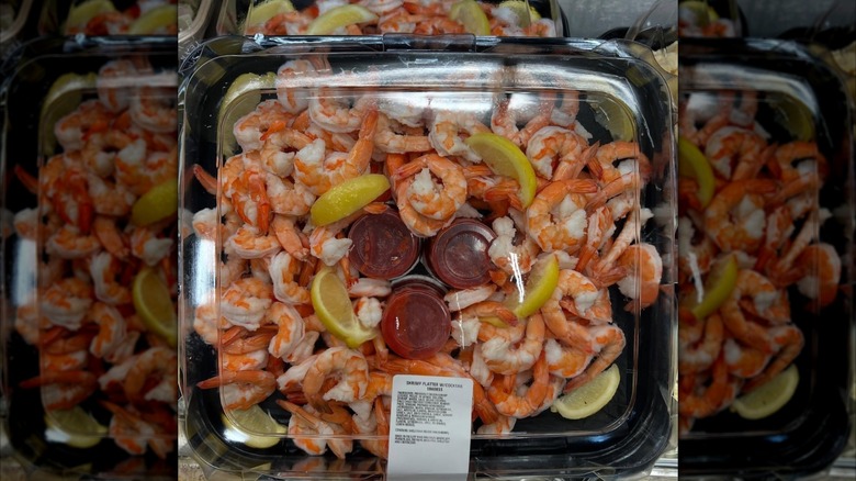 Plastic tray of shrimp cocktail with lemon wedges and three pots of cocktail sauce