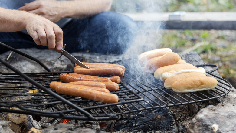 Hands preparing hot dogs over a wood-fire grill