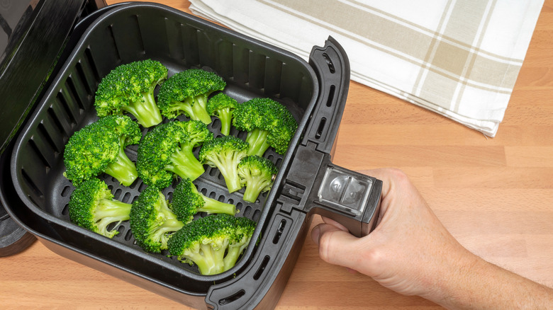 Hand pulling out air fryer basket full of broccoli florets