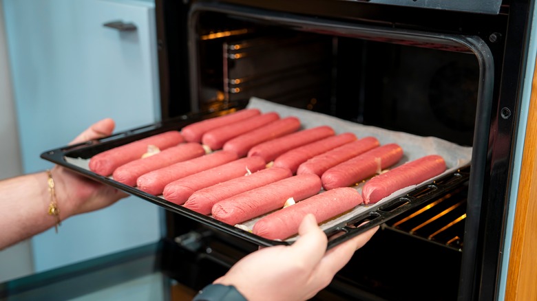 Hands placing sheet pan of hot dogs in the oven