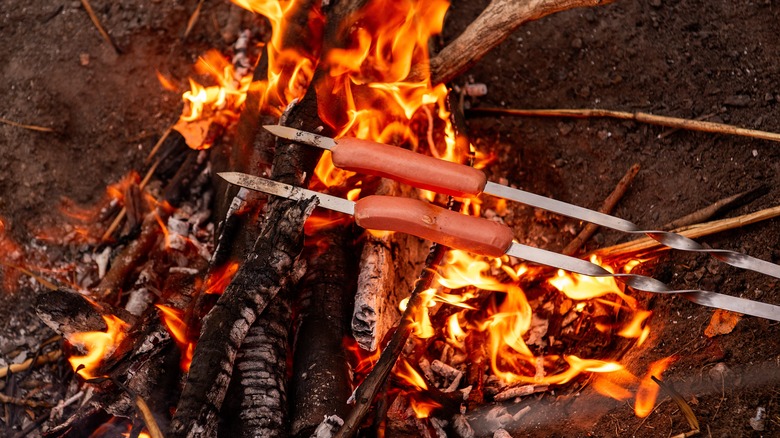 Two sausages on metal skewers over flames