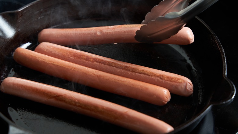 Hot dogs in a frying pan being turned over with tongs
