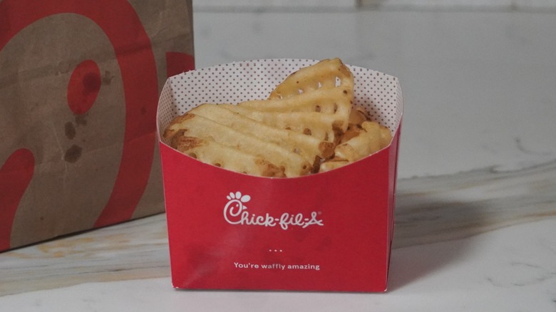 Chick-fil-A French fries next to a brown paper Chick-fil-A bag.