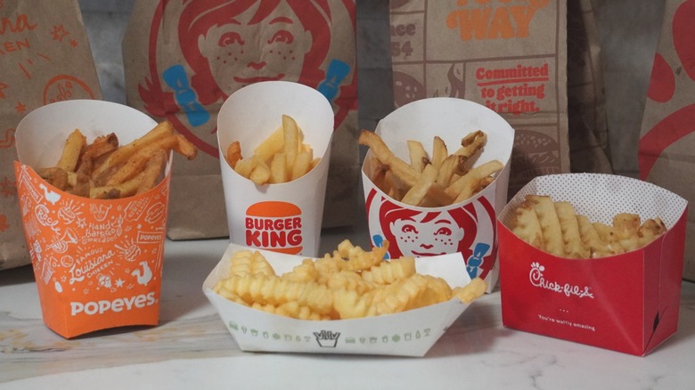 French fries from Popeyes, Burger King, Shake Shack, Wendy's, and Chick-fil-A (left to right) in front of brown paper fast food bags.