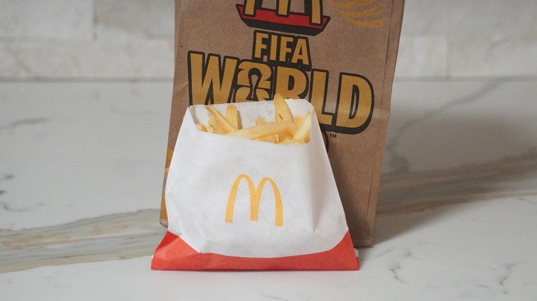 McDonald's French fries in front of a brown paper McDonald's bag.