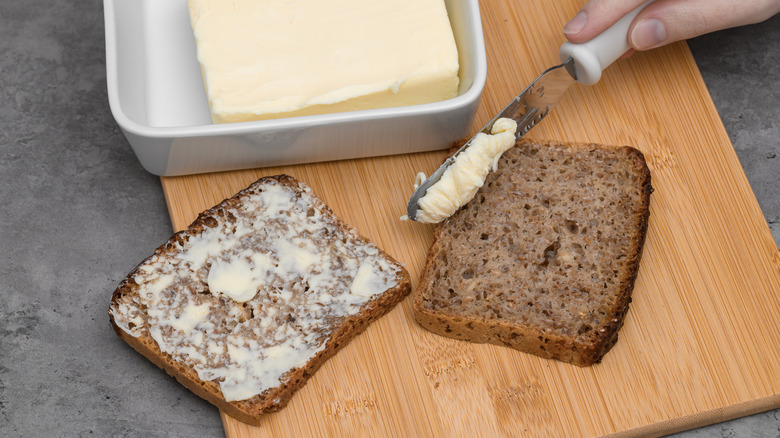 Hands hold and butter a piece of bread.