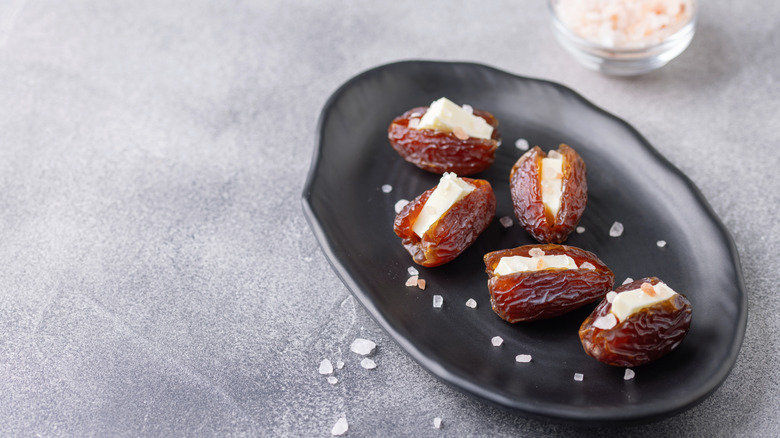 Butter-stuffed dates sit on a black plate near a ramekin of flaky salt