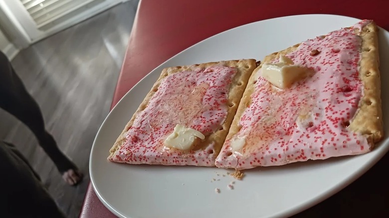 Frosted Pop-Tarts with pats of butter melting on them sit on a white plate.