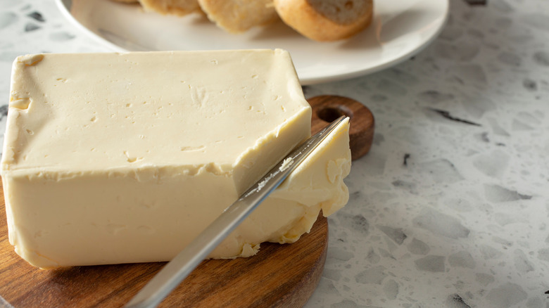 A knife cuts into a block of butter sitting on a wooden cutting board