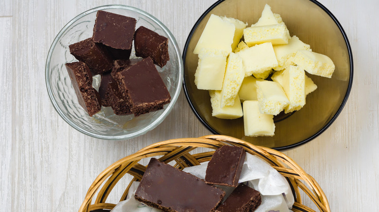 Squares of chocolate in a bowl and basket sit next to a bowl of butter pats
