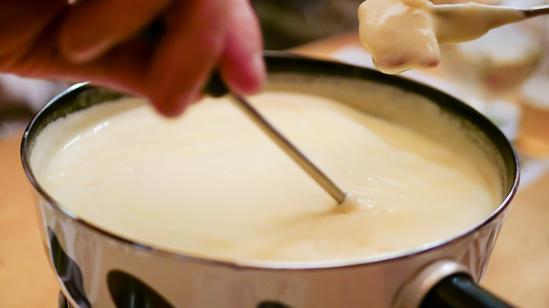 A fondue pot with cheese inside and people dipping into it