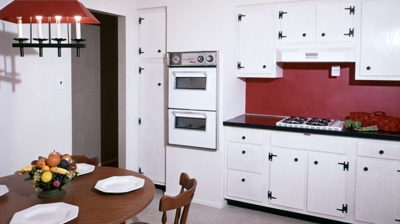 A 1970s kitchen with white double wall ovens and a white range top
