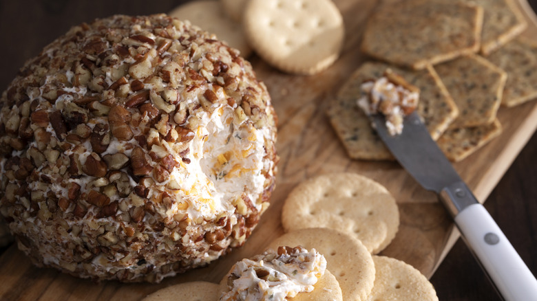 Macro shot of a nut crusted cheeseball with crackers on a board