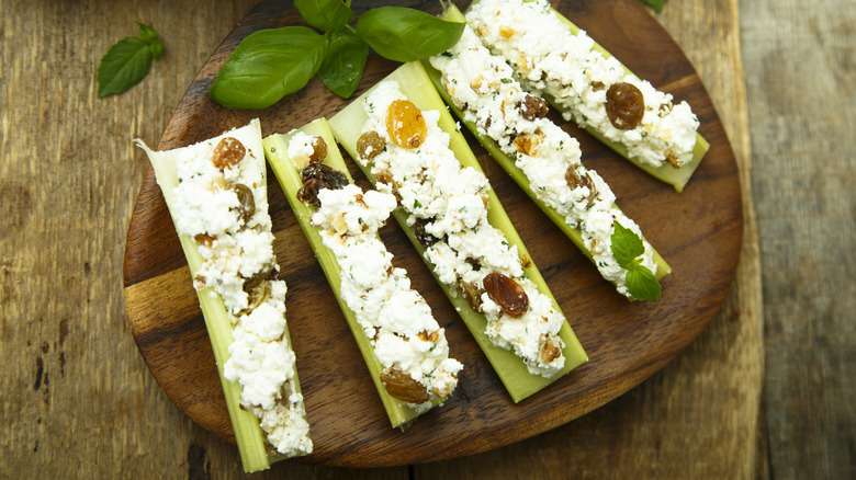 A wooden plate filled with celery stuffed with cottage cheese and raisins