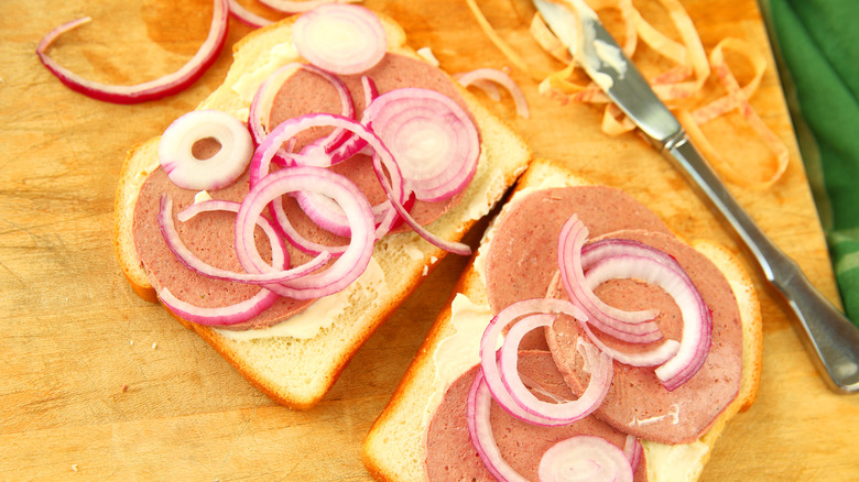 Open-faced sandwiches topped with slices of braunschweiger, butter, and slices of raw red onion on a wooden cutting board