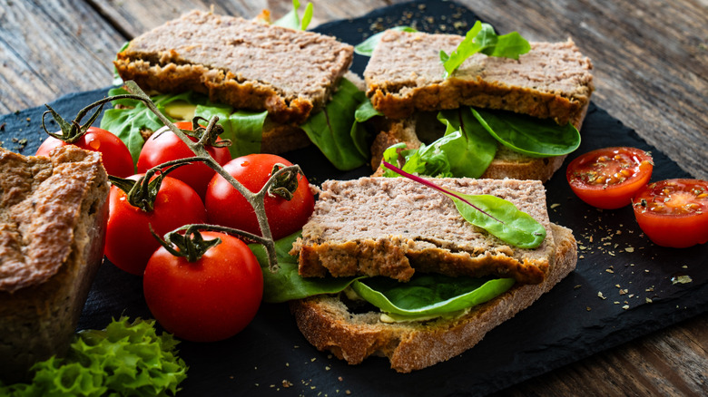 Open-faced liverwurst sandwiches with arugula and tomatoes on black slate slab