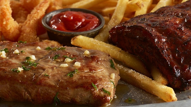 A Ruby Tuesday steak sits on a plate with ribs, french fries, and ketchup