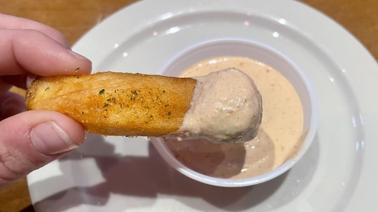 Hand holding steak fry dipped in Texas Roadhouse Cajun horseradish sauce