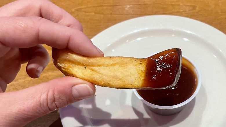 Hand holding steak fry dipped in Texas Roadhouse BBQ sauce