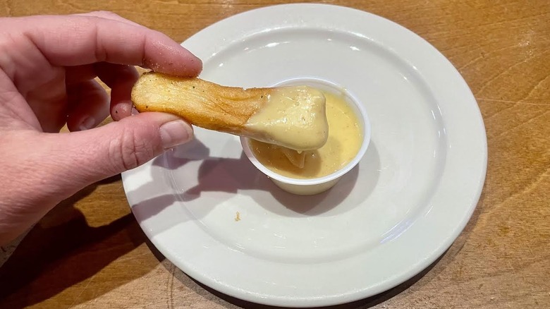 Hand holding steak fry dipped in Texas Roadhouse honey mustard