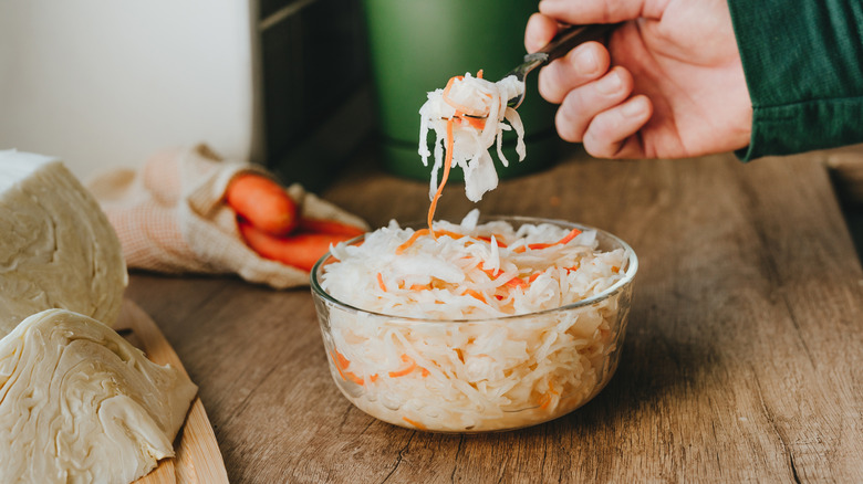 A hand ready to eat a forkful of fermented shredded carrot and sauerkraut