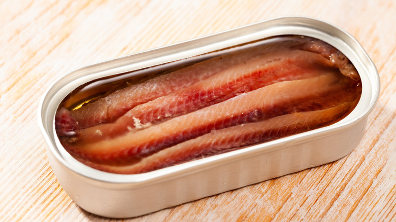 Open can of tinned anchovies on a wooden counter top