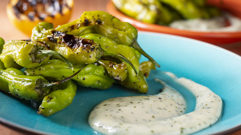 Upclose shot of plated blistered shishito peppers with a creamy dipping sauce