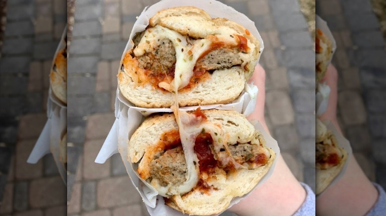 A large meatball sub is cut in two and held outside the restaurant