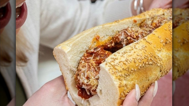 A half meatball sub is held near a person's face at PrimoHoagies