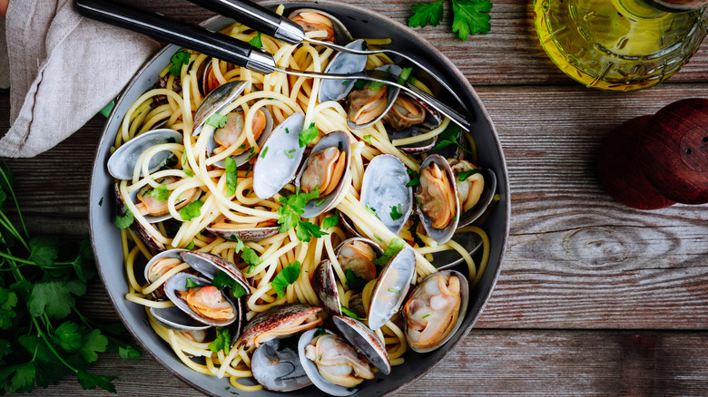 A plate of clams and pasta sits on a wooden table