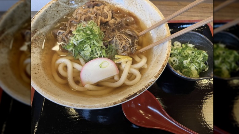 Udon noodles on a black tray with a red spoon
