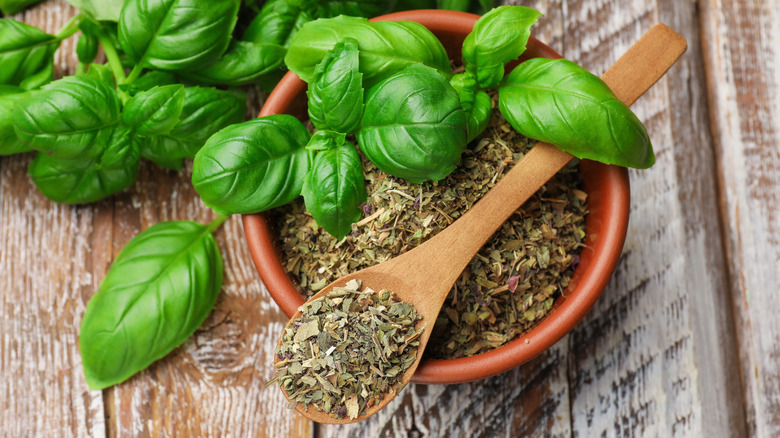 Closeup of a bowl of dried Italian seasonings with fresh basil nearby