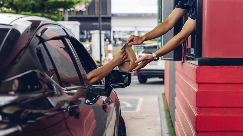Hand from a car is receiving a drive-thru order from an employee