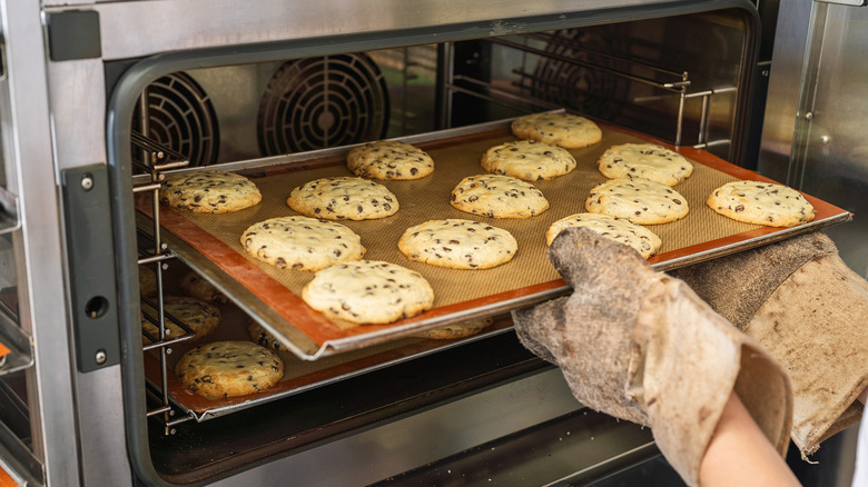 A person removes a baking tray with cookies from an oven