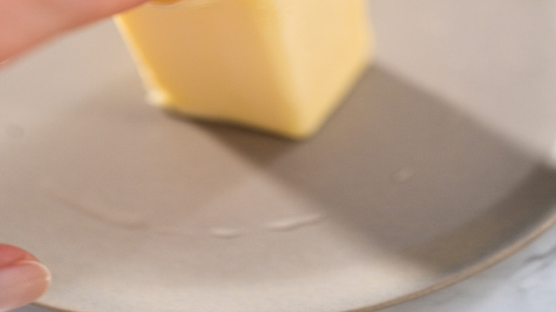 A person's finger presses against softened butter