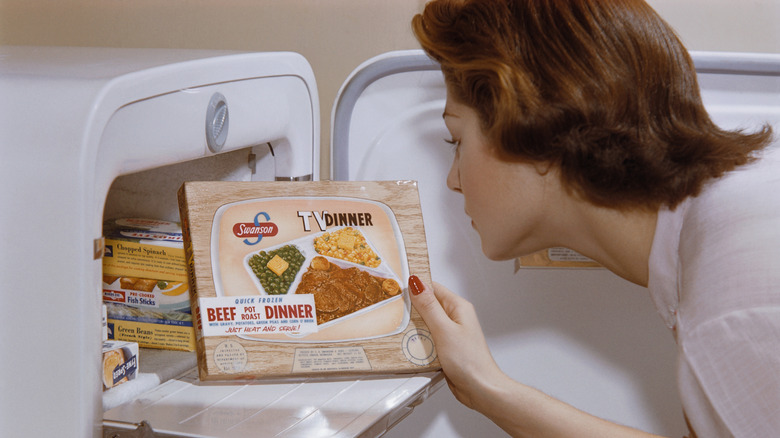 A woman retrieving a TV dinner from the freezer compartment of a 1950s fridge