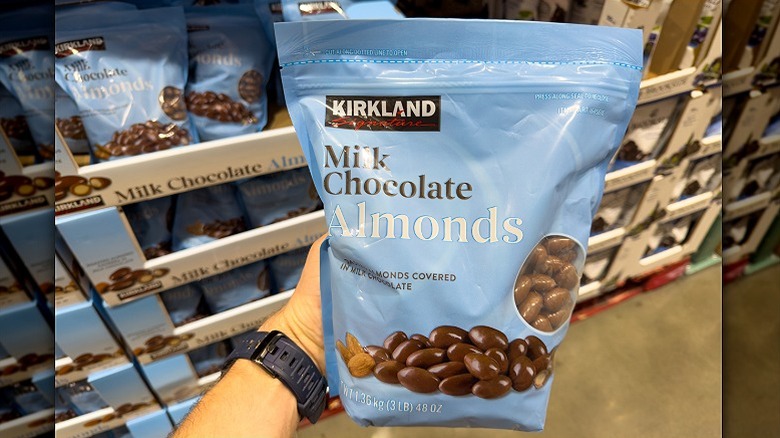 A person holds a bag of Costco Milk Chocolate Almonds in the candy aisle